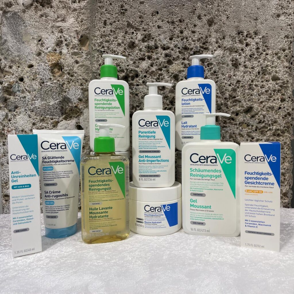 Verschiedene Apotheken-Produkte in unterschiedlichen Verpackungen und Größen, angeordnet auf einer Marmoroberfläche vor einem grauen Stein-Hintergrund.