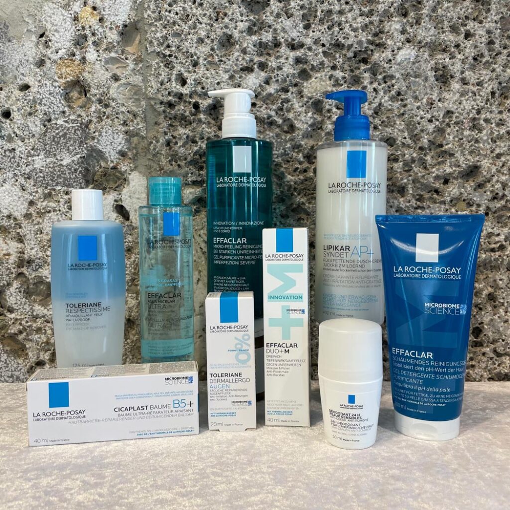 Verschiedene Apotheken-Produkte in unterschiedlichen Verpackungen und Größen, angeordnet auf einer Marmoroberfläche vor einem grauen Stein-Hintergrund.