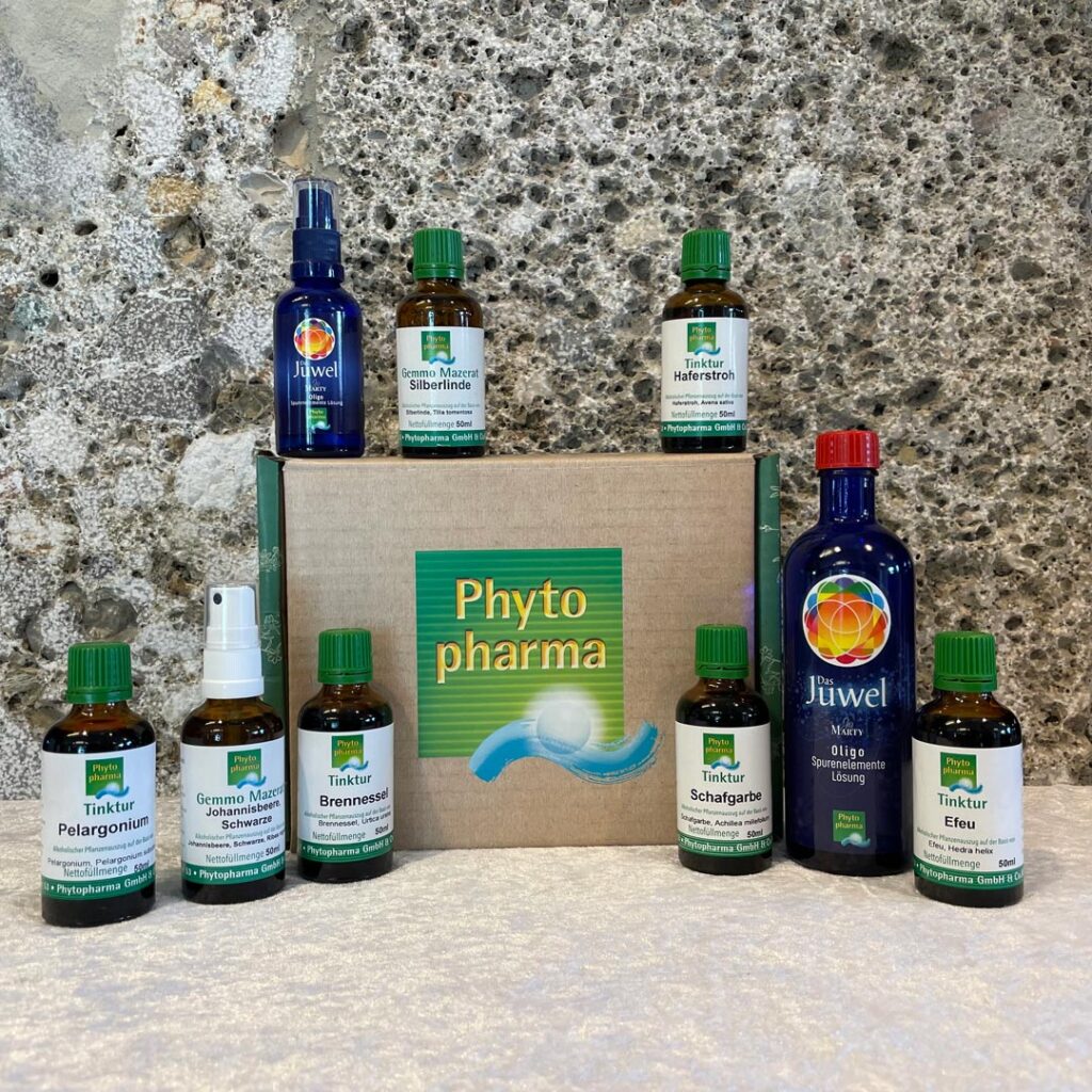 Verschiedene Apotheken-Produkte in unterschiedlichen Verpackungen und Größen, angeordnet auf einer Marmoroberfläche vor einem grauen Stein-Hintergrund.