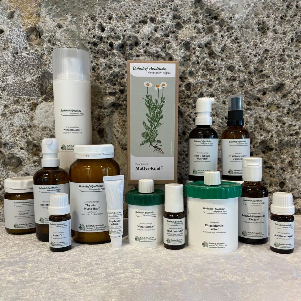 Verschiedene Apotheken-Produkte in unterschiedlichen Verpackungen und Größen, angeordnet auf einer Marmoroberfläche vor einem grauen Stein-Hintergrund.